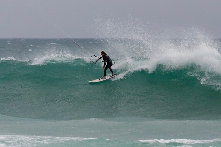 man kitesurfing in the water, surfboard in shot with white wave wash