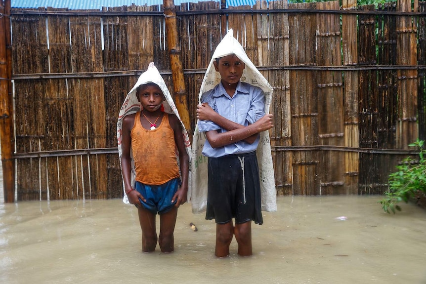 Two boys stand with makeshift plastic covers in knee-deep floodwater