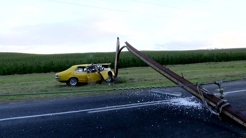 A car crumpled against a power pole which has split and fallen.