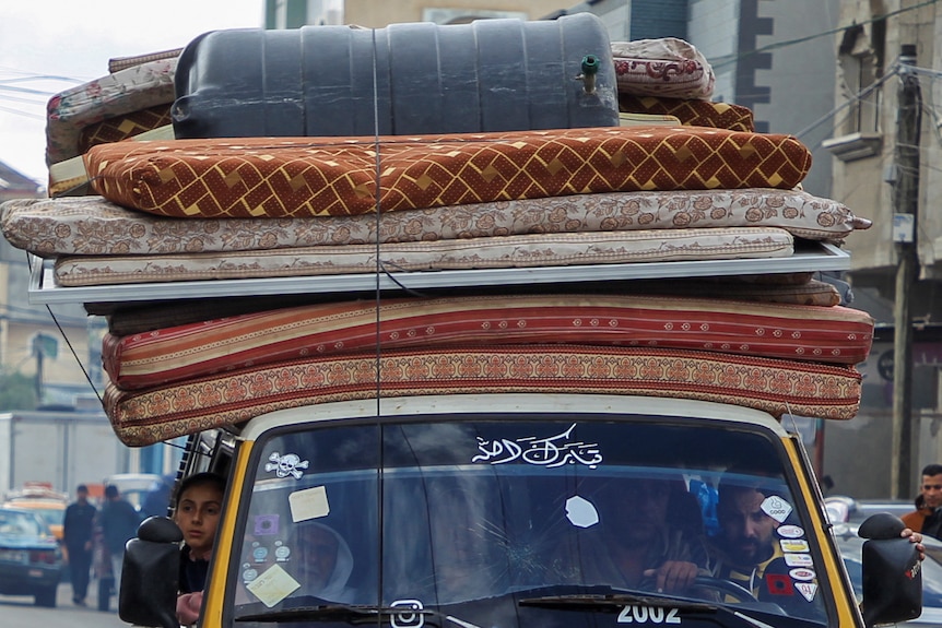 A bundle of mattresses atop a taxi cab 
