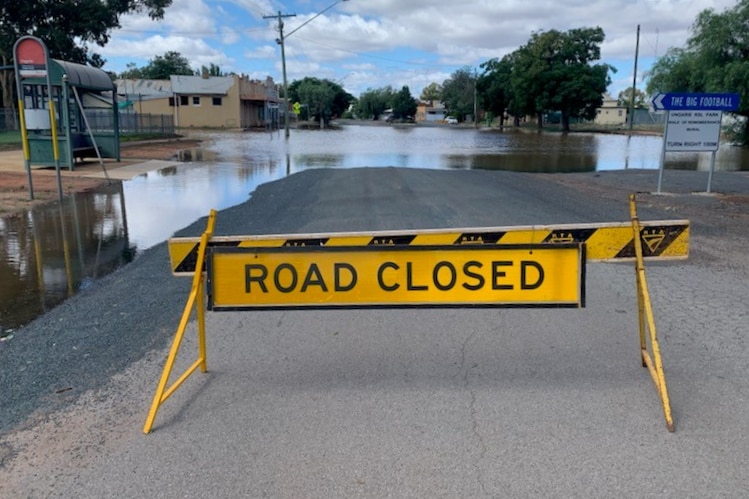 A yellow hazard sign reading "road closed" blocks a road ahead of floodwater