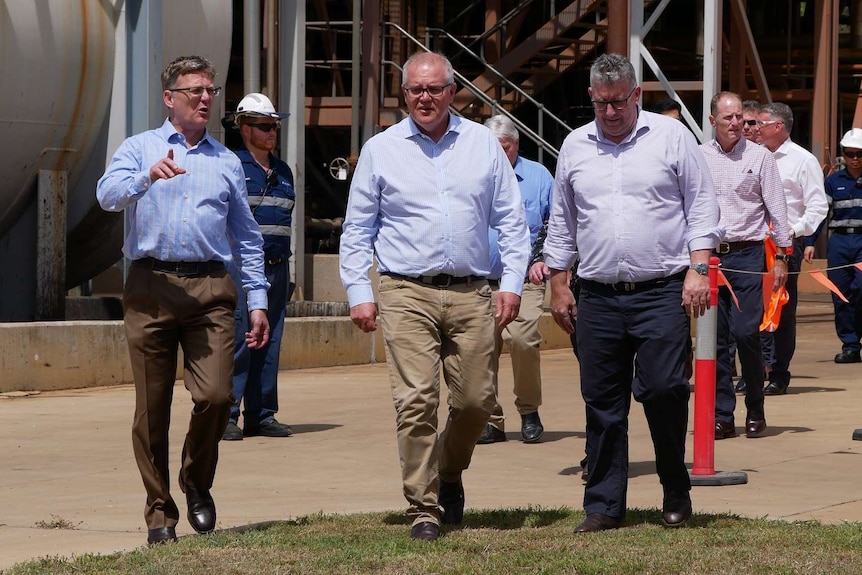 A group of men walk in a line around an industrial site.