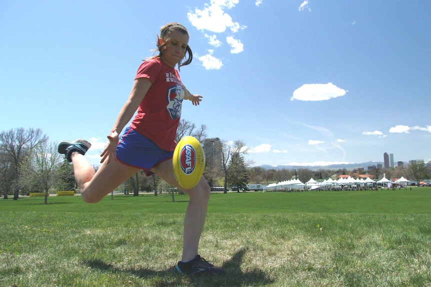 Sara Edwards Rohner kicks a football with snow-capped mountains in the background.