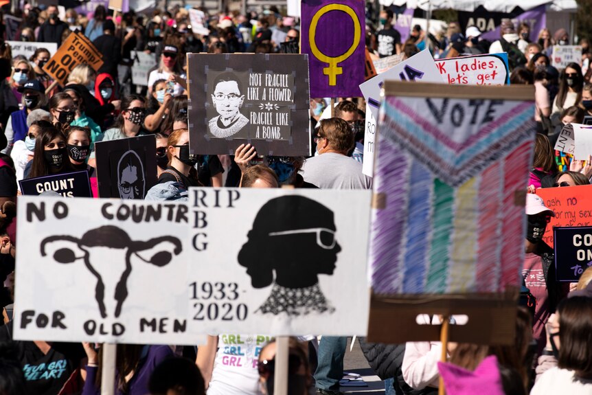 Demonstrators at a rally hold up sign with Ruth Bader Ginsburg on them