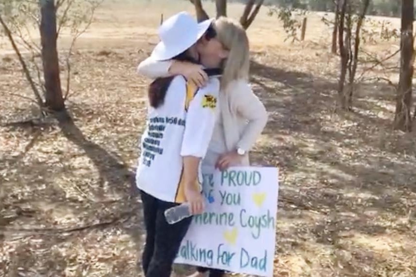 Two women hug while one holds a sign.