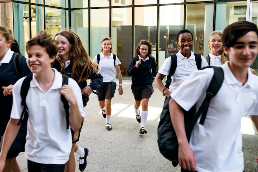 Happy high school students in school uniform walking out of school