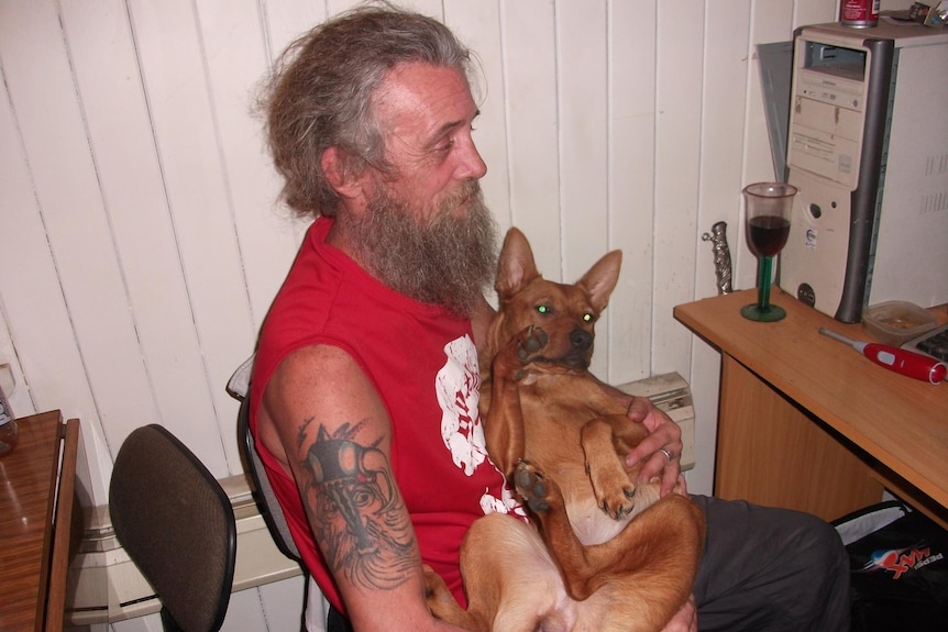 man in red shirt with arm tattoo sitting at desk holding dog