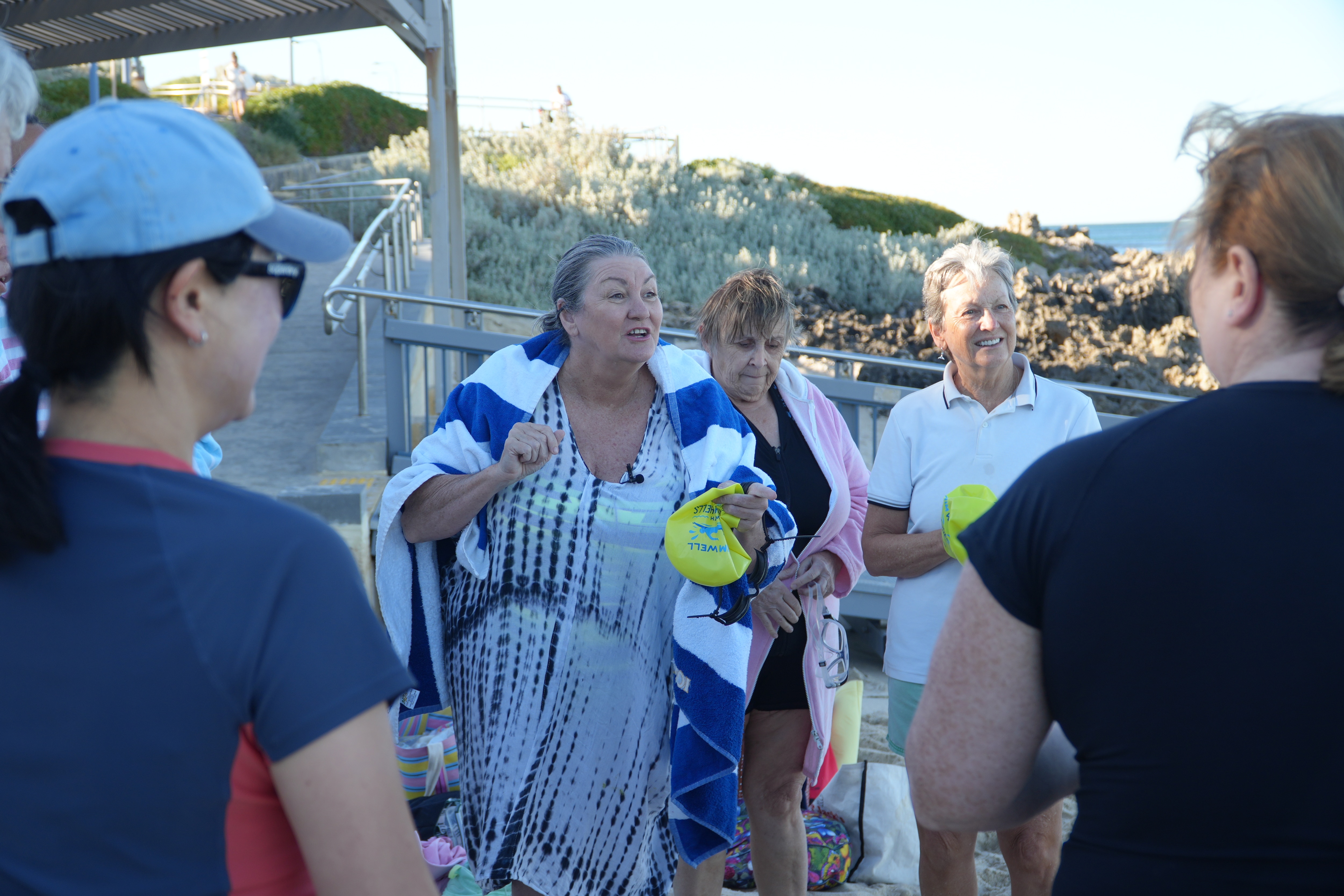 Shelley sorri e olha para um grupo de pessoas à beira-mar.
