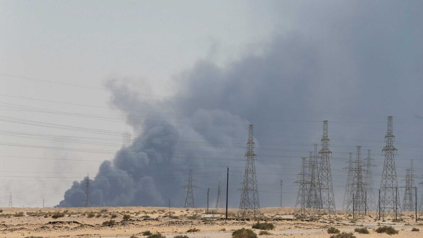 Looking across a Saudi Arabian desert field, you electric cable towers as the horizon is blanketed by dark grey smoke.