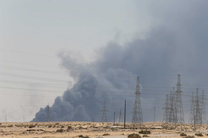 Looking across a Saudi Arabian desert field, you electric cable towers as the horizon is blanketed by dark grey smoke.