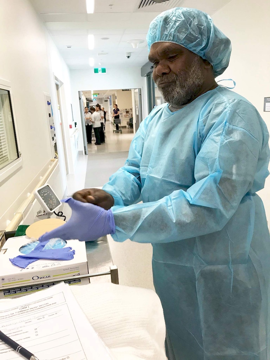 Anangu healer, Cyril Mckenzie putting purple surgery gloves on.
