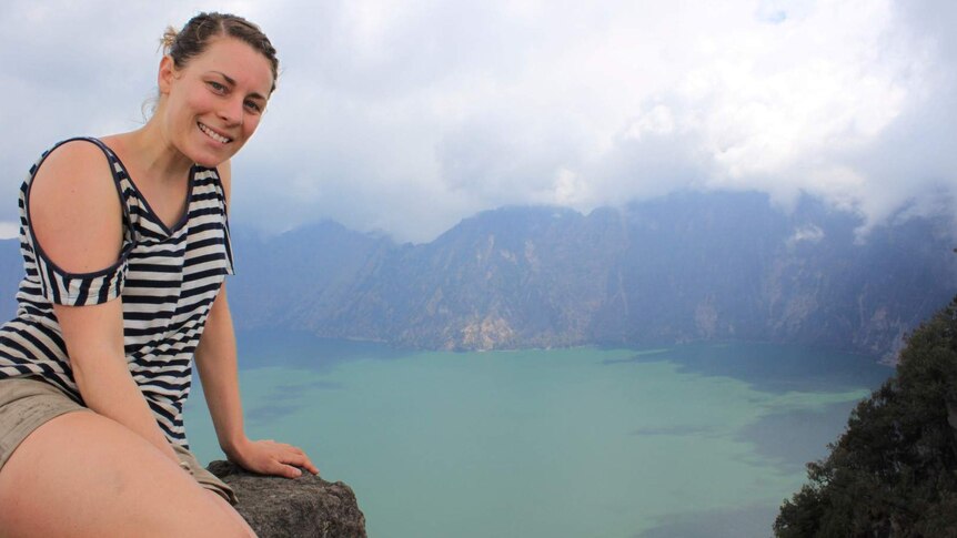 Sarah is sitting on a rock and smiling while overlooking a vast lake in the background.