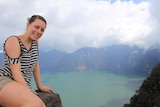 Sarah is sitting on a rock and smiling while overlooking a vast lake in the background.