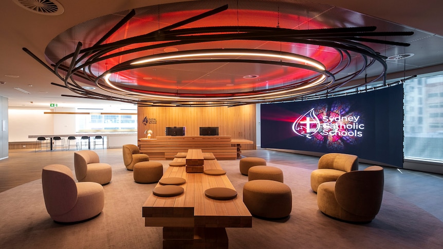 An office waiting area with a reception desk and the words 'Sydney Catholic Schools' on a TV screen.