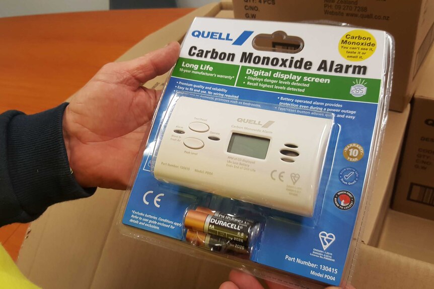 A person holds a carbon monoxide alarm on its packaging
