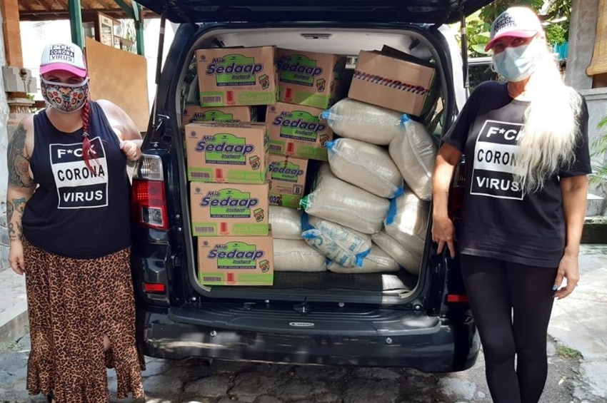 Two Australian women wearing a mask next to a car filled with boxes of instant noodles and rice.