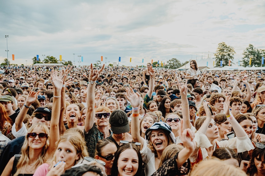 A crowd of young Groovin The Moo festival-goers raise their hands and cheer.