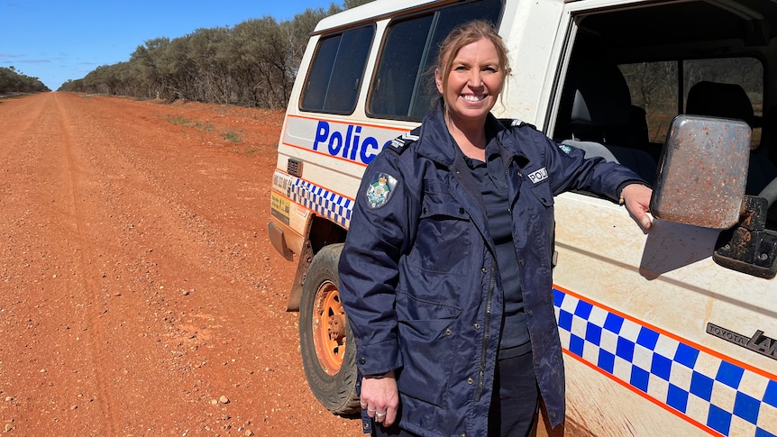 Police officer Lea Macken standing in the outback in front of a police car.