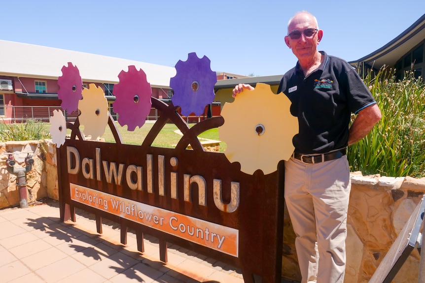 A man standing beside a sign saying 'Dalwallinu' with cut out still flowers above it..