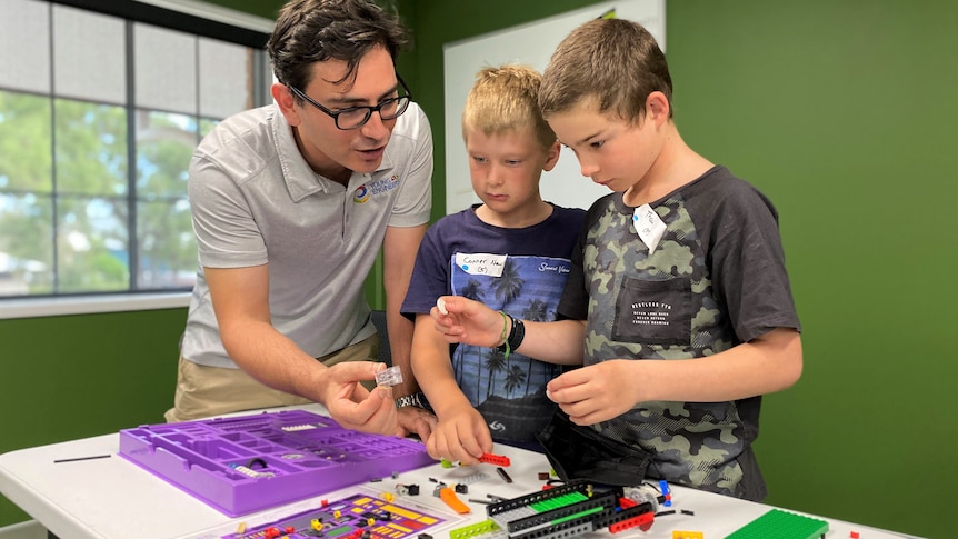 Two boys and a man are building model machines with plastic bricks. 