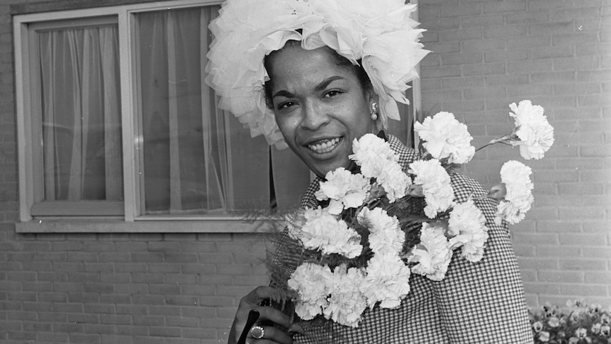 A monochrome shot of Della Reese wearing a floral hat and carrying white roses