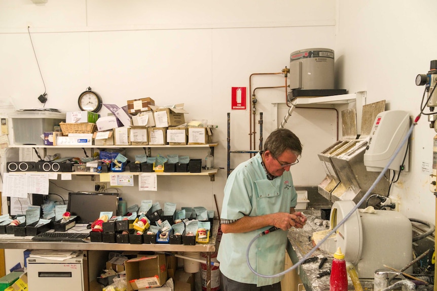 A man looks down as he works at a denture clinic, with many boxes and items surrounding him.