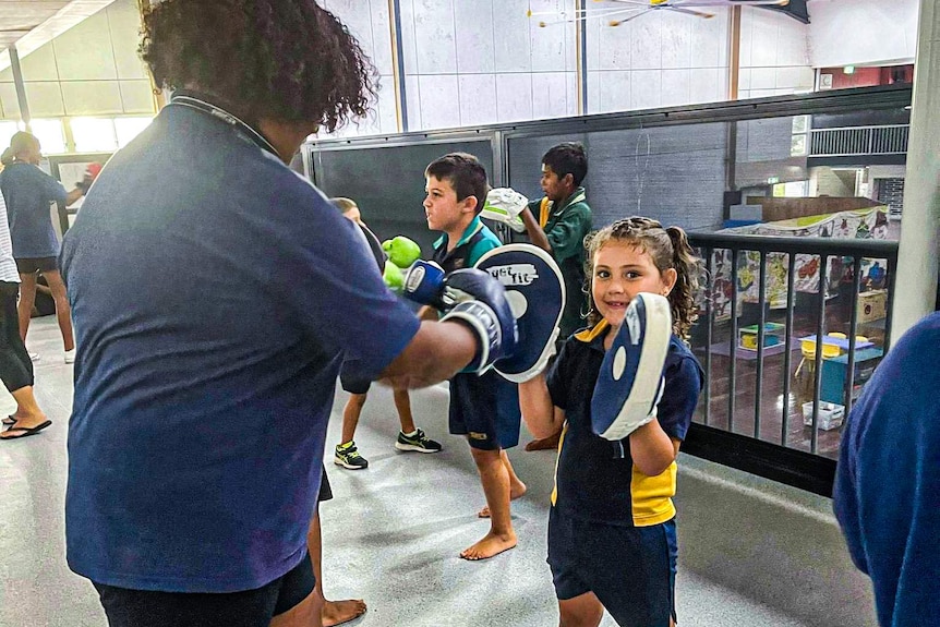 A secondary school student and a smaller primary school student training with boxing pads.