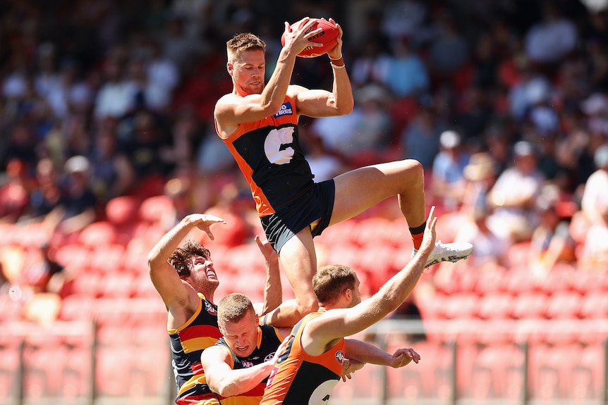 An AFL player uses an opposition player's shoulder to balance as he looks down while grabbing the ball in both hands. 