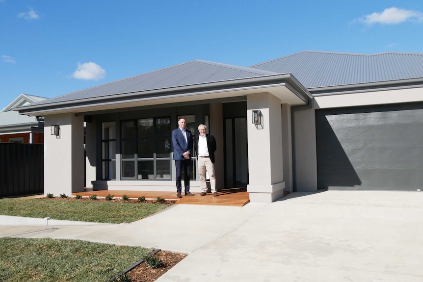 Two men stand in front of a new home.