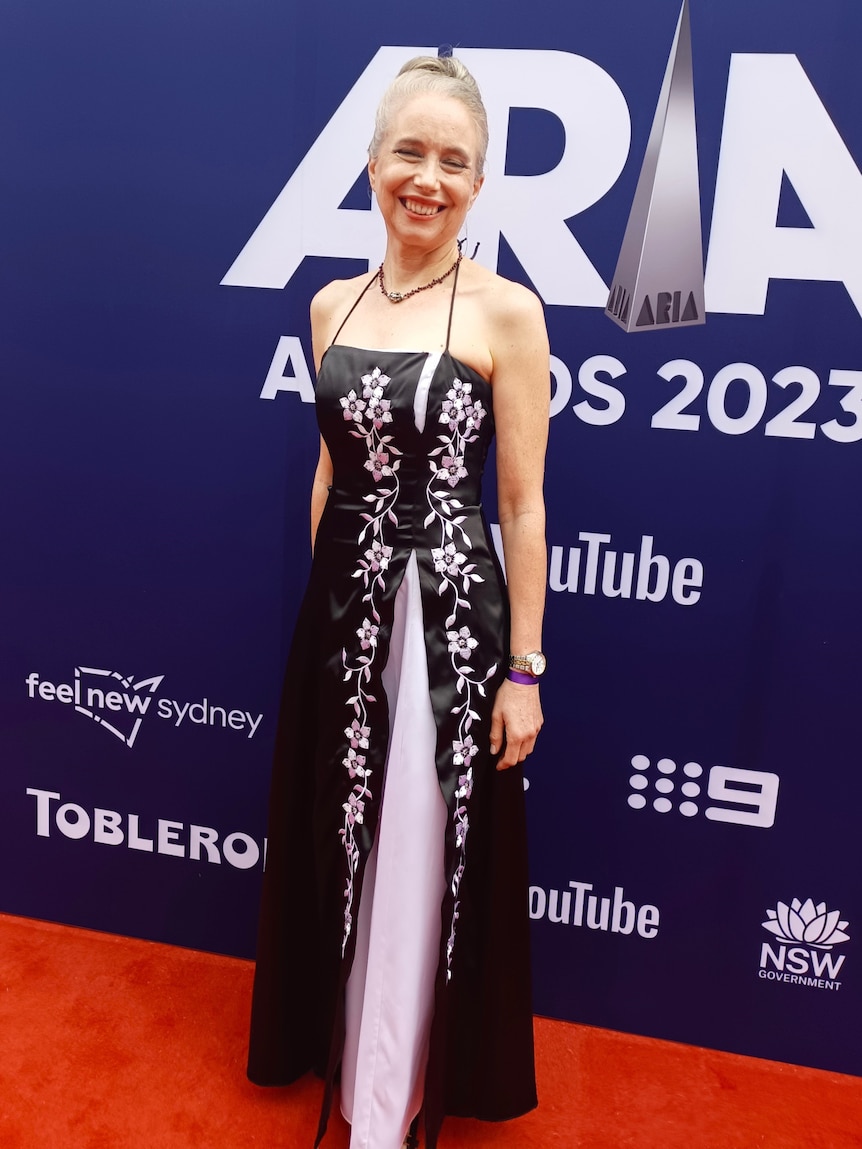 A smiling, middle-aged woman in a dark dress stands on the red carpet at the ARIA Music Awards.