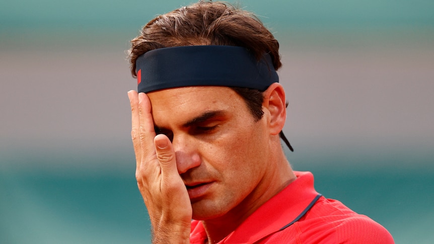 A Swiss male tennis players wipes his face with his right hand at the French Open.