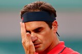 A Swiss male tennis players wipes his face with his right hand at the French Open.