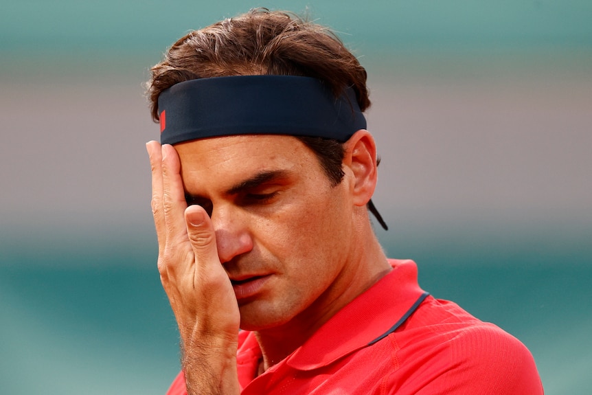 A Swiss male tennis players wipes his face with his right hand at the French Open.