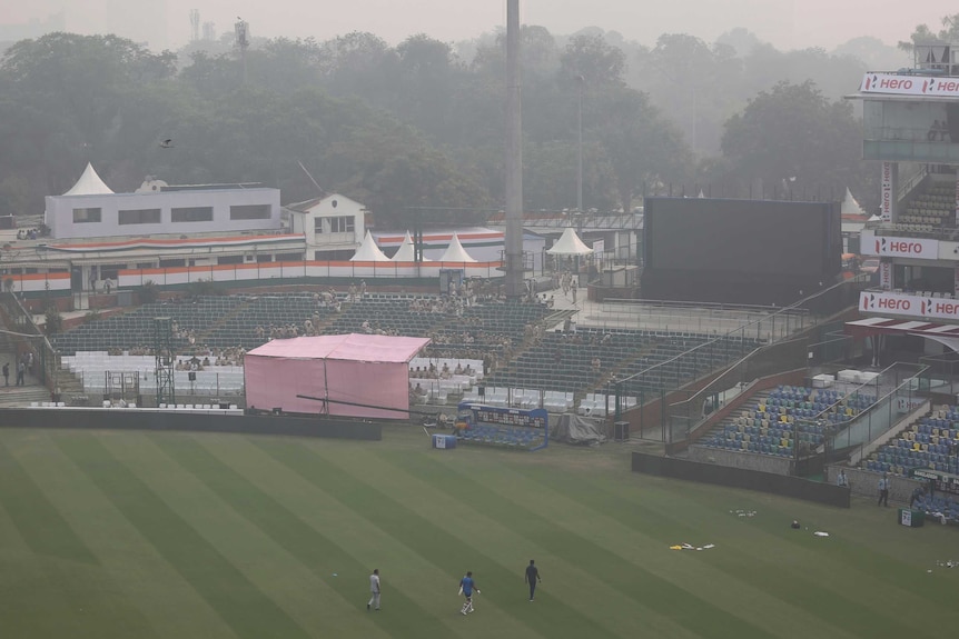 Cricket players walk off a field covered with smog