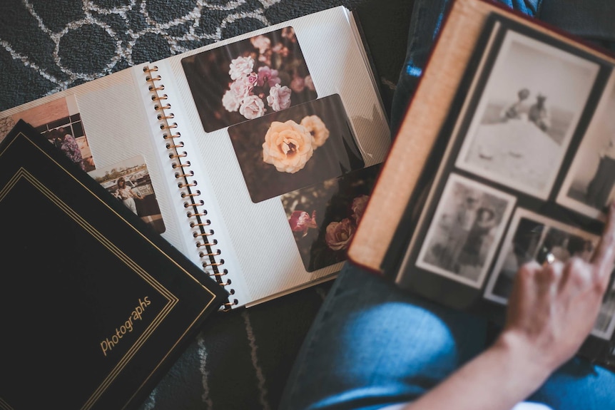 Two photo albums with old photos in them open with a young woman's hand pointing at a photo