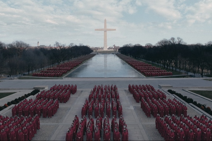 Handmaids line up in rows ahead of the Washington Monument recreated as a crucifix