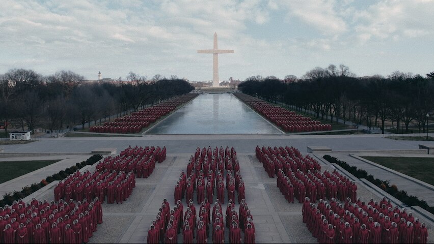 Handmaids line up in rows ahead of the Washington Monument recreated as a crucifix