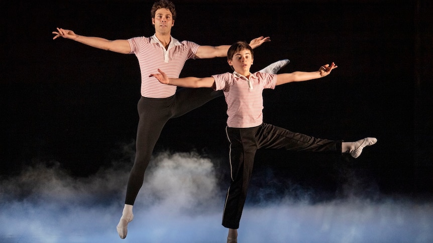 Aaron Smyth and child performer Wade Neilsen perform a dance move wearing identical black pants and collared short-sleeved shirt