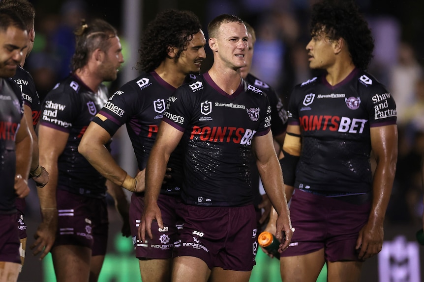 A group of professional rugby league players wearing dark jerseys stand in a group