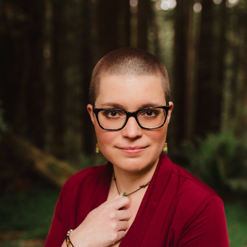 Woman with glasses, shaved head and red top in a forest