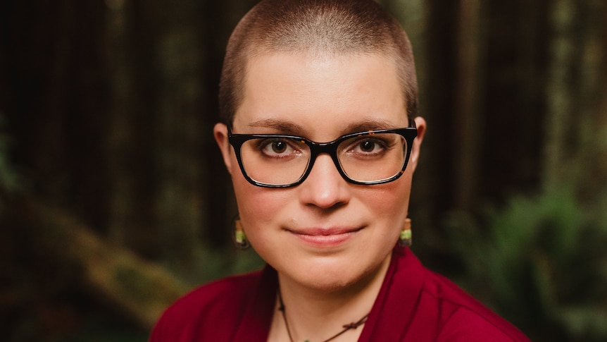 Woman with glasses, shaved head and red top in a forest