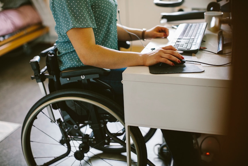 Woman in a wheelchair wearing a green polka dot top can be seen at a computer desk. 