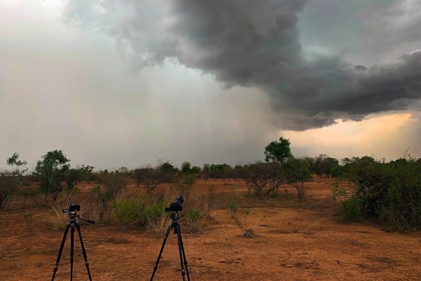 Two tripods with cameras capturing a storm in the distance