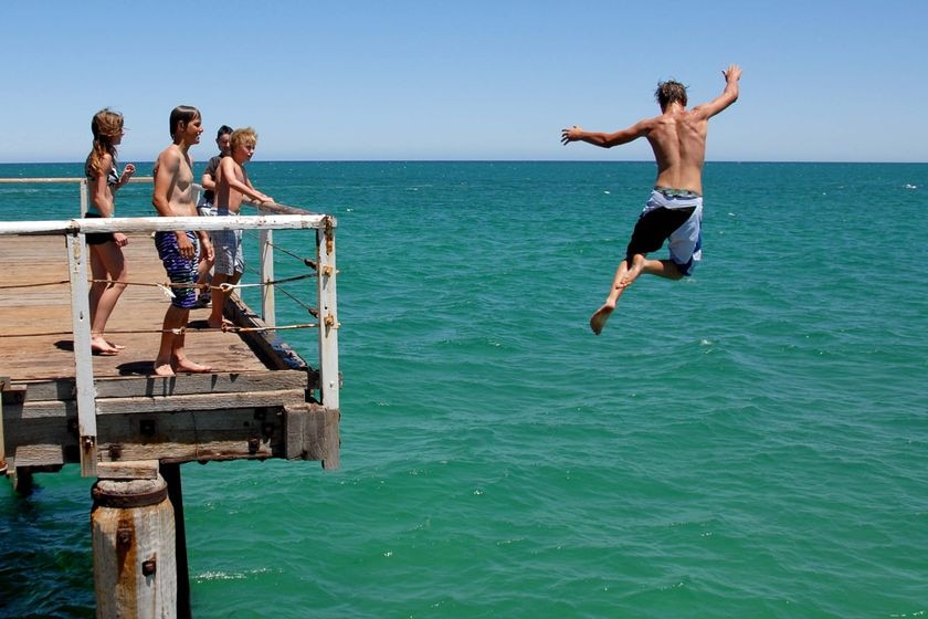 Teenage boy jumps off jetty into ocean.