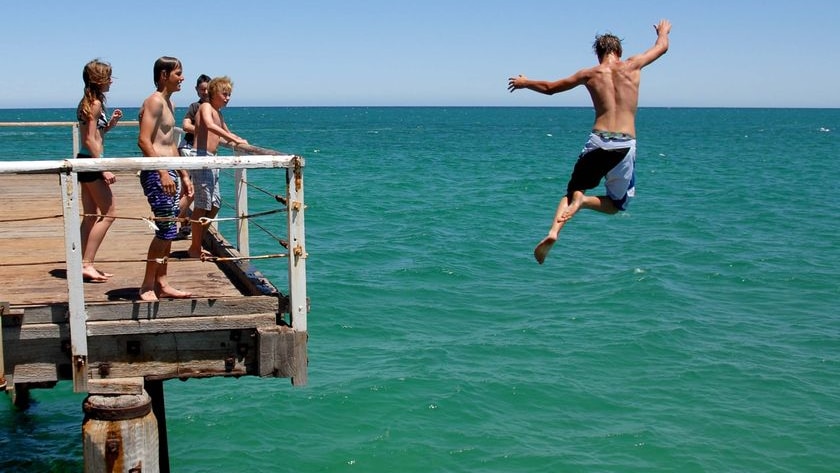 Teenage boy jumps off jetty into ocean.