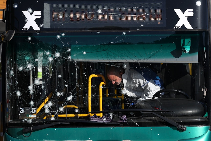 A police officer inspect a bus with a windscreen damaged in an explosion.