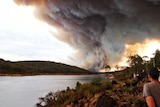 People sitting at the Mundaring Weir watch thick plumes of smoke from a fire go into the sky.