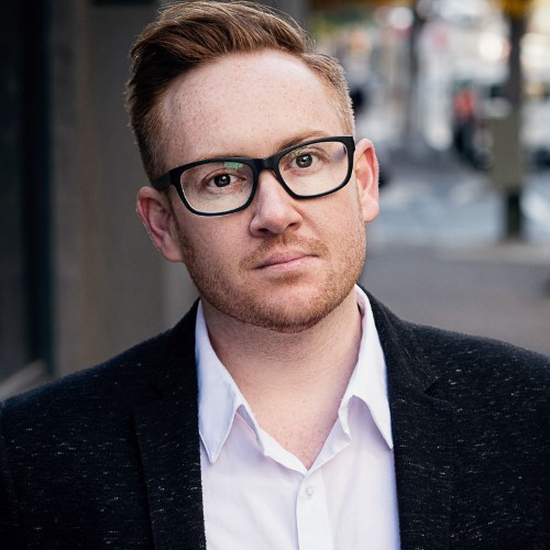 Jay James-Moody, a red-haired white man in his late 30s, wearing glasses, a white shirt and black blazer.