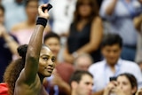 Serena Williams holds her hand up to acknowledge the crowd at the US Open as she carries her tennis bag off court.