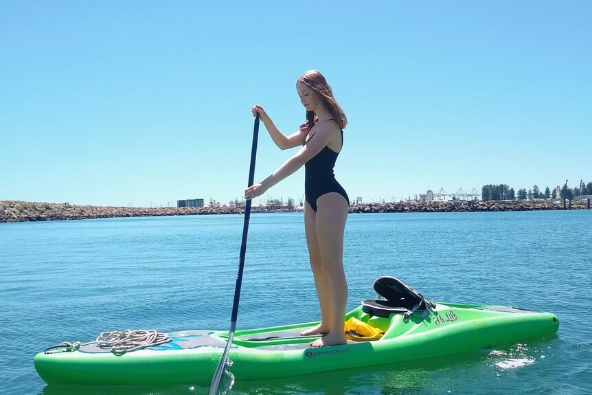 Chanelle Willems wears a black bathing suit while standing on a stand-up paddle board.